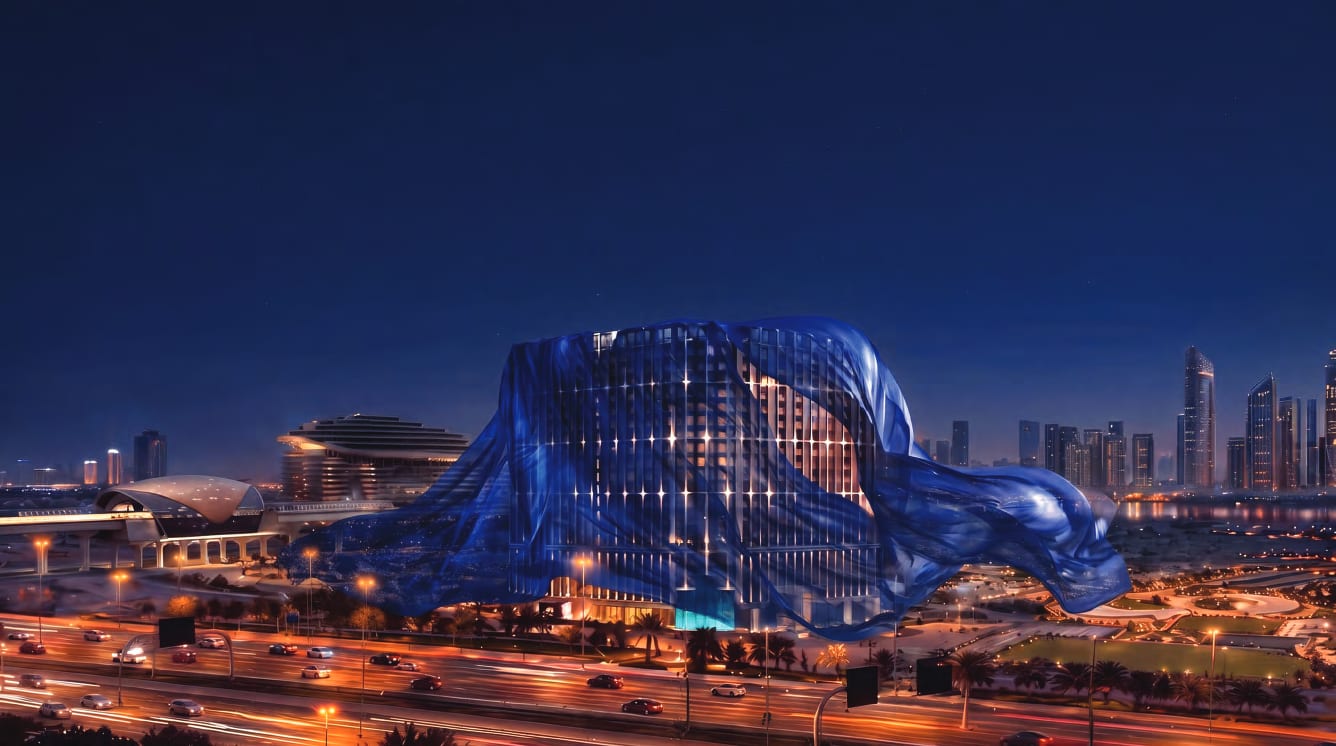 Binghatti Starfall at night, its lit façade partly veiled in blue fabric above a busy road, with the Dubai skyline behind